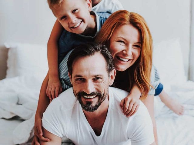 Smiling man and woman laying on bed with kids